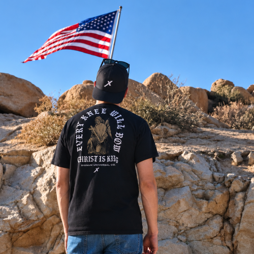 Man wearing Black Every Knee Will Bow Catholic Shirt, back print of angel at the cross. Model is 5'11" and wearing a Large