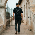Man wearing Black Thy Kingdom Come Catholic Shirt, back print, walking through a church arch